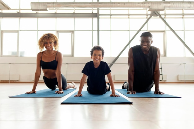 La joven familia atlética afroamericana yace y descansa sobre una estera de yoga en el gimnasio, mamá, papá e hijo.