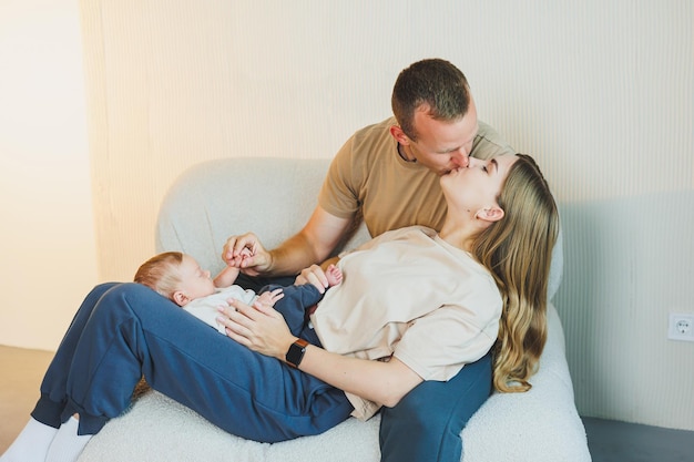 Una joven familia con un bebé recién nacido una madre y un padre felices besando a su hijo padres y un niño sonriente en sus brazos
