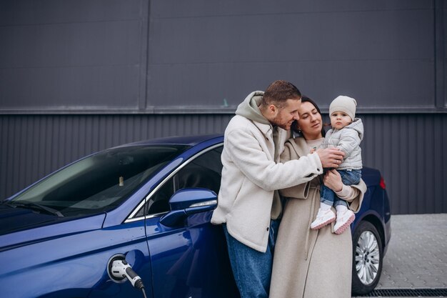 Una joven familia feliz carga un auto eléctrico