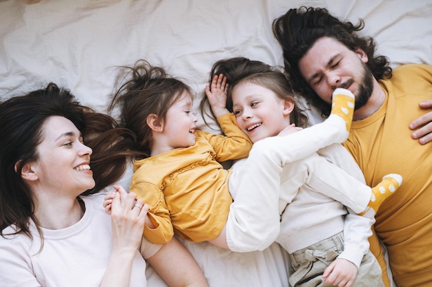 Joven familia feliz con dos niñas en la cama en la acogedora casa vista desde arriba