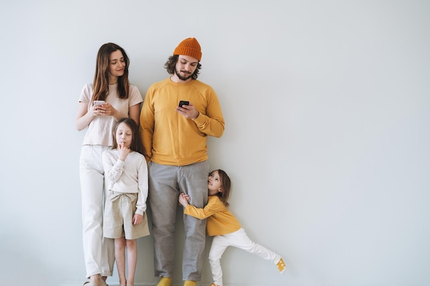 Joven familia feliz con dos niños niñas sobre fondo de pared gris padres usando teléfonos móviles