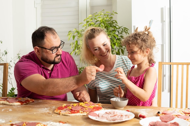 La joven familia feliz está cocinando pizza casera.