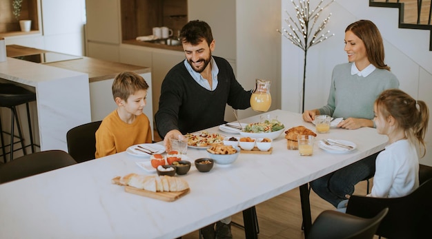 Joven familia feliz hablando mientras desayuna en la mesa del comedor en el apartamento