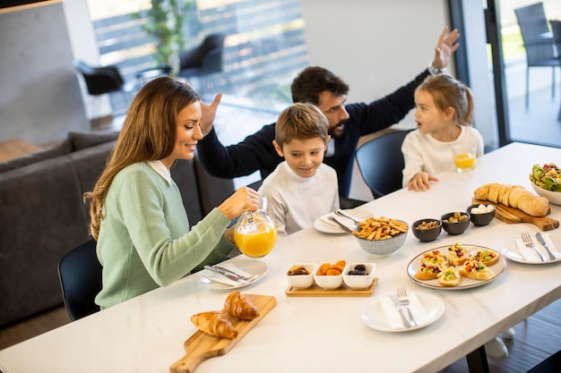Joven familia feliz hablando mientras desayuna en la mesa del comedor en el apartamento