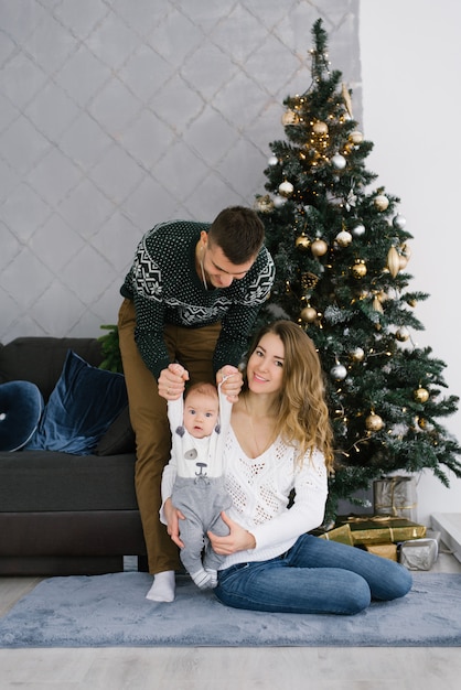 Una joven familia feliz con un hijo pequeño se sienta en el suelo cerca de un árbol de Navidad en la sala de estar. H