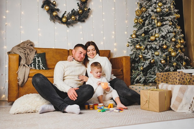 Una joven familia feliz con un niño pequeño está celebrando el Año Nuevo en casa cerca del árbol de Navidad Navidad con la familia tiempo de Año Nuevo para celebrar