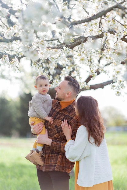 Foto una joven familia feliz pasa el tiempo en el parque de primavera en flor mamá, papá y el hijo pequeño están jugando afuera