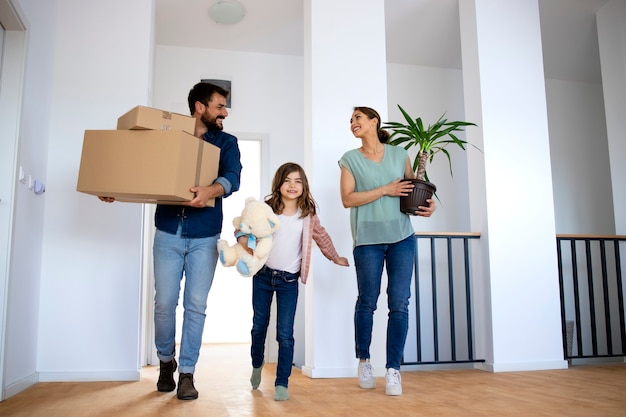 Joven familia feliz sosteniendo cajas y flores mientras se muda a casa nueva.