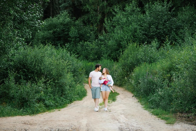 Una joven familia feliz con su hijo en brazos camina por un sendero forestal y disfruta