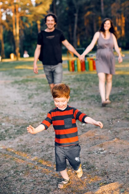 Joven familia feliz con su hijo pequeño está caminando en un parque de verano y riendo