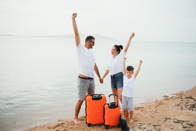 Foto joven familia feliz con su hijo y sus maletas en la playa