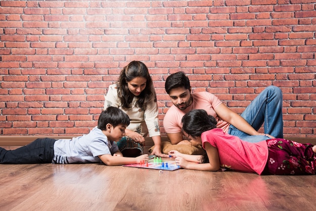 Joven familia india de cuatro jugando juegos de mesa como ajedrez, Ludo o Snack and Ladder en casa en cuarentena
