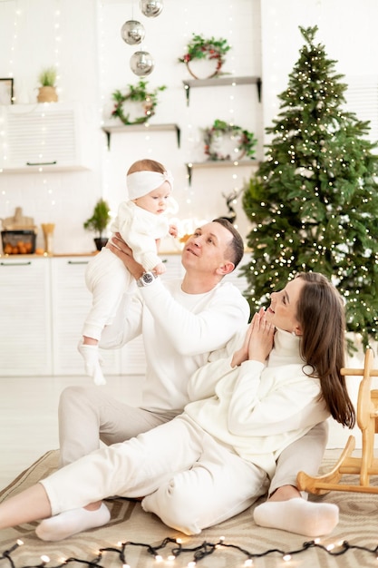 una joven familia con un niño pequeño está disfrutando del año nuevo en el árbol de Navidad en la cocina o en una casa brillante sonriendo besándose y abrazándose felicitándose unos a otros celebra la fiesta