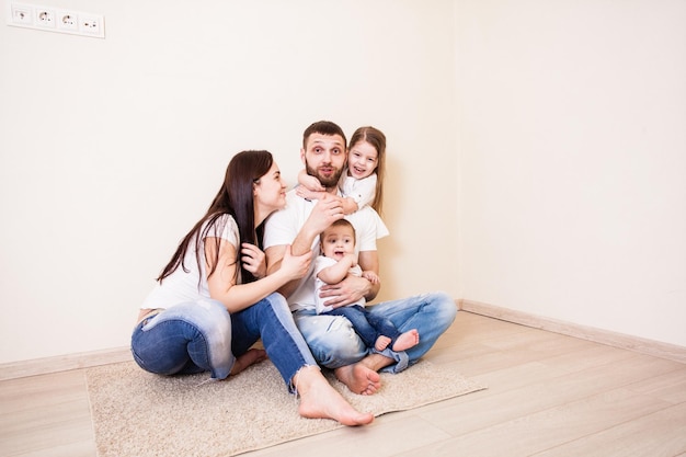 La joven familia: papá, mamá y dos niños sentados en el suelo