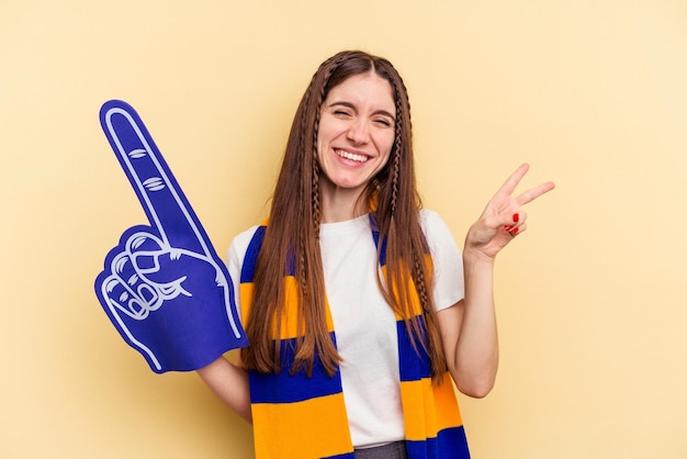 Joven fanática de los deportes aislada de fondo amarillo alegre y despreocupada mostrando un símbolo de paz con los dedos