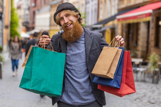 Joven feliz adicto a las compras consumidor después de la venta de compras con bolsas llenas caminando por la calle de la ciudad