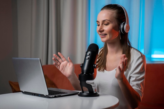 Una joven feliz y alegre con auriculares y un micrófono profesional está grabando un podcast de audio