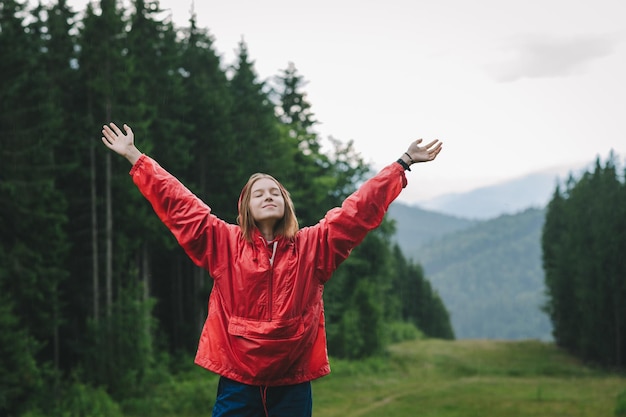 Una joven feliz y alegre con un impermeable rojo levanta las manos