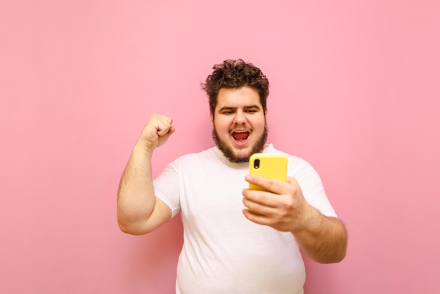 Joven feliz con barba y sobrepeso apuesta en deportes y gana aislado en rosa