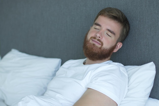 Joven feliz barbudo hombre guapo somnoliento yacía en la cama en el dormitorio en casa en la madrugada sonrisa y