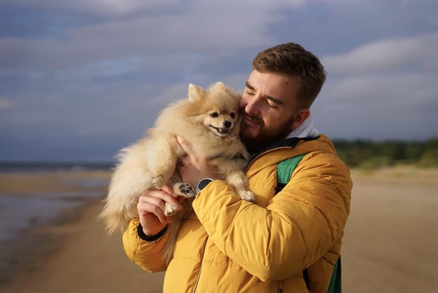 Foto joven feliz caminando con su mascota pomeranian spitz perro en la playa sostener cachorro en las manos de la gente