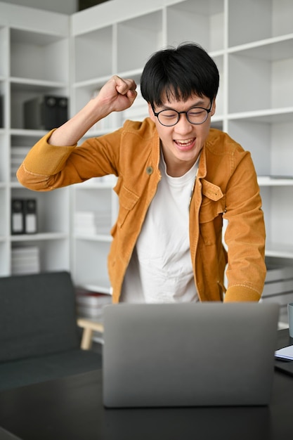 Un joven feliz celebra consigo mismo mirando la pantalla de un portátil