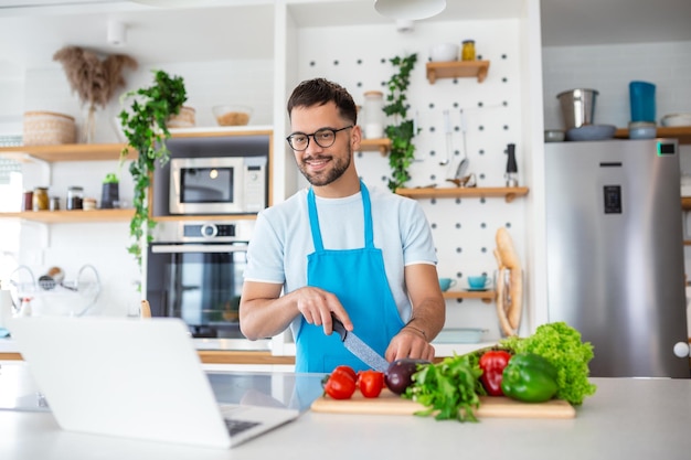 Un joven feliz cocinando una cena saludable en casa Está siguiendo un video tutorial en la laptop