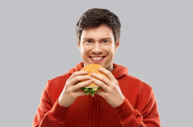 Un joven feliz comiendo una hamburguesa.