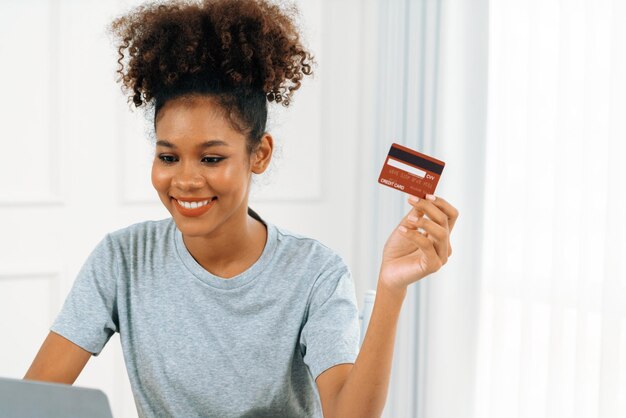 Una joven feliz compra productos comprando en línea en casa mientras pide artículos desde Internet con un sistema de pago en línea con tarjeta de crédito protegido por una seguridad cibernética crucial desde la plataforma de la tienda en línea