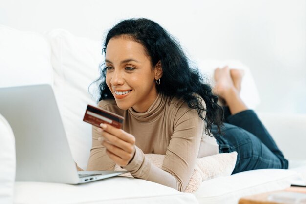Una joven feliz compra productos comprando en línea en casa mientras pide artículos desde Internet con un sistema de pago en línea con tarjeta de crédito protegido por una seguridad cibernética crucial desde la plataforma de la tienda en línea