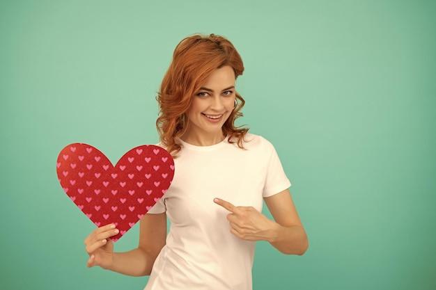 joven feliz con corazón rojo en fondo azul señala el dedo