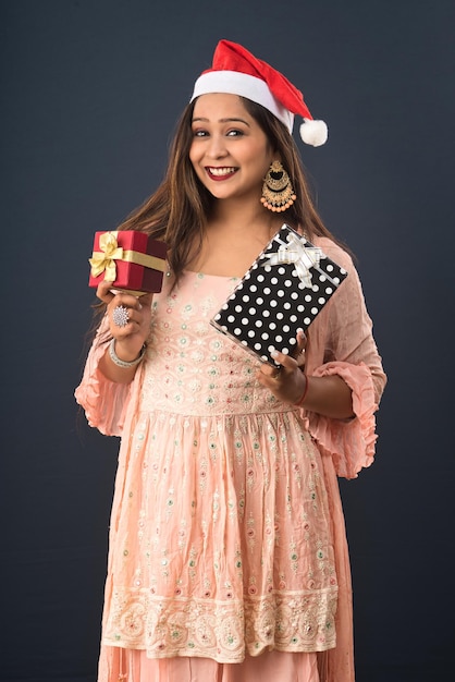 Una joven feliz y emocionada con un sombrero de Papá Noel con cajas de regalo sobre un concepto de Navidad de fondo gris