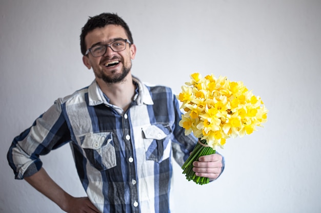 Un joven feliz con gafas y una camisa con un ramo de narcisos. El concepto de saludos y día de la mujer.