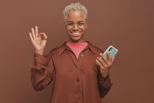 Joven feliz hermosa mujer afroamericana con teléfono muestra gesto ok