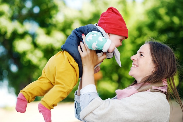 Joven y feliz madre con su pequeño hijo jugando con él en el verano en el parque