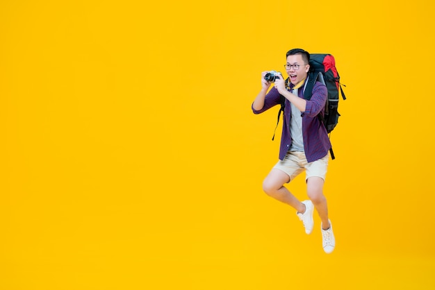 Joven feliz mochilero masculino asiático tomando fotos mientras salta al lado del espacio de copia