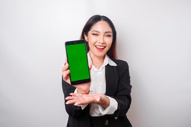 Una joven y feliz mujer de negocios lleva un traje negro que muestra espacio para copiar en su teléfono aislado de fondo blanco