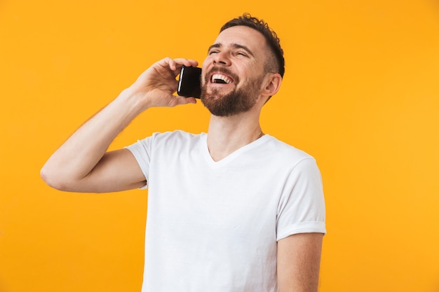 Joven feliz posando aislado sobre pared amarilla hablando por teléfono