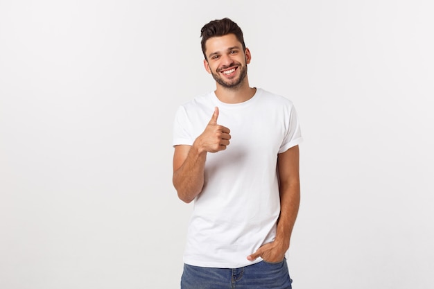 Joven feliz con pulgares arriba firmar en eventuales aislados en la pared blanca