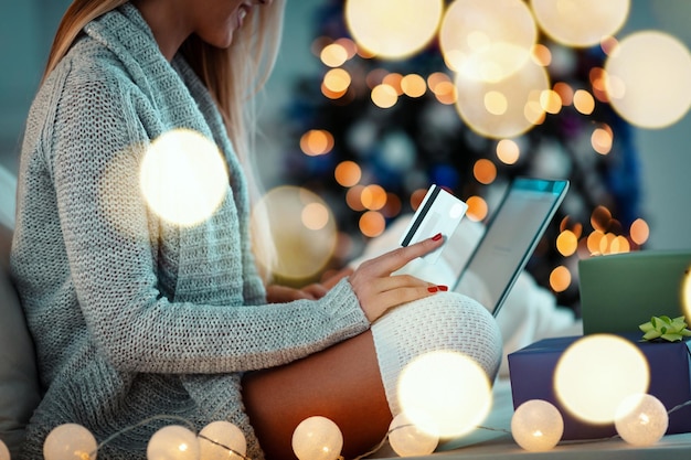 Foto una joven feliz se relaja en casa y compra regalos de navidad con una laptop en línea.