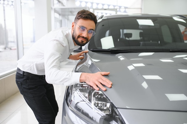 Un joven feliz revisando un nuevo auto de lujo comprando un automóvil en el centro del concesionario