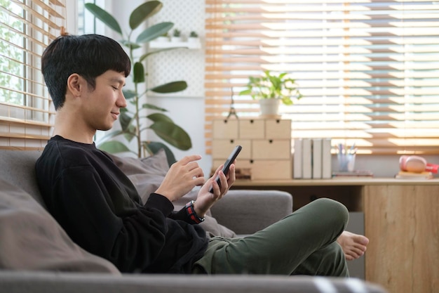 Joven feliz revisando las redes sociales o comprando en línea en un teléfono inteligente