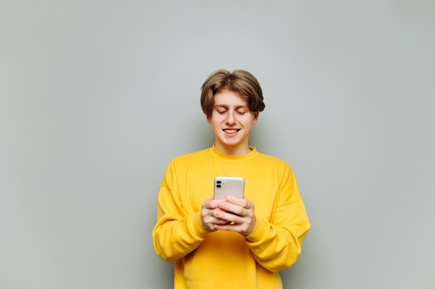 Un joven feliz con ropa amarilla usa un teléfono inteligente con un fondo gris