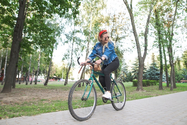 Joven feliz en ropa elegante monta una bicicleta verde en el parque.