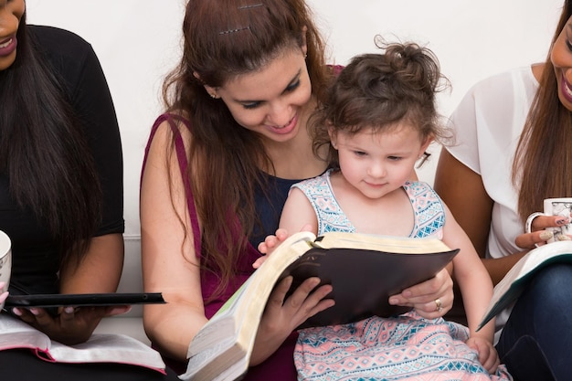 Una joven feliz sentada leyendo un libro con su hija en casa.