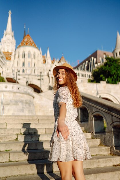 Una joven feliz con sombrero al amanecer disfruta de la vista de hermosos edificios Concepto de turismo de estilo de vida