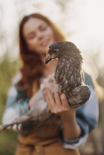 Una joven feliz sonríe mientras mira a la cámara y sostiene una gallina joven que pone huevos para su granja a la luz del sol El concepto de aves de corral cuidadosas y saludables Foto de alta calidad