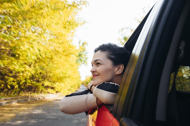 Una joven feliz y sonriente mirando por la ventana del auto mientras viaja