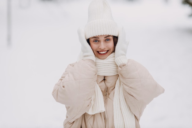 Una joven feliz y sonriente se pone un sombrero de bufanda y guantes disfruta del clima invernal en el parque invernal nevado