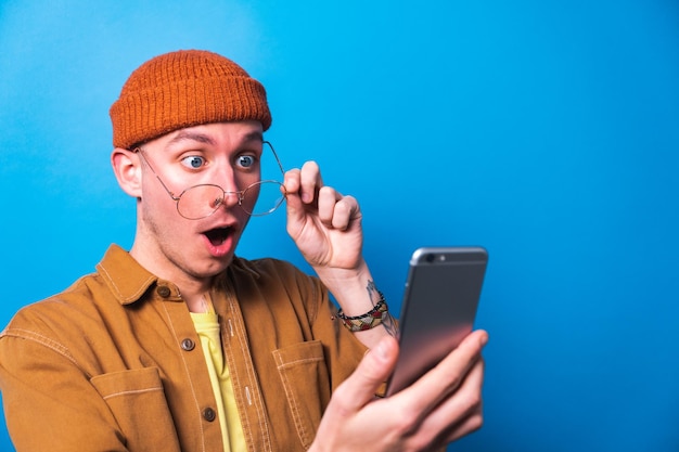 Joven feliz sorprendido celebrando usando una aplicación de teléfono inteligente con fondo azul